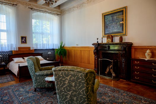 Chambre du Château de Sainte-Julie avec lit, fauteuils, cheminée et décoration élégante.