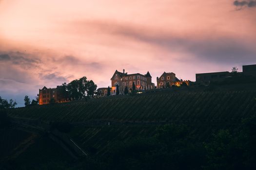 Château illuminé au crépuscule, entouré de vignes, offrant un cadre romantique en région.