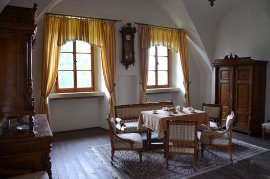 Salle de séjour élégante avec table, chaises en bois, horloge murale et fenêtres aux rideaux jaunes au Château de Sainte-Juli