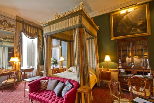 Chambre élégante du Château de Sainte-Julie avec lit à baldaquin, canapé rouge et mobilier ancien.